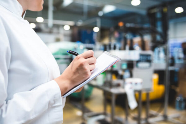 Young happy female worker in a lab writing notes about appraisal of equipment.