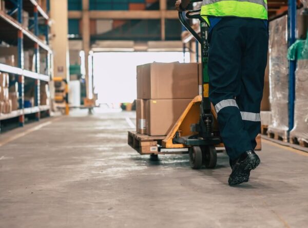 Warehouse staff moving lab equipment with hand lift while walking through warehouse.