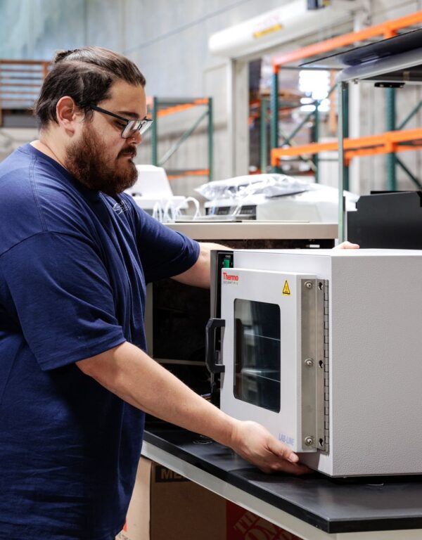 Technician performing a detailed assessment of lab equipment for resale potential in a warehouse setting.
