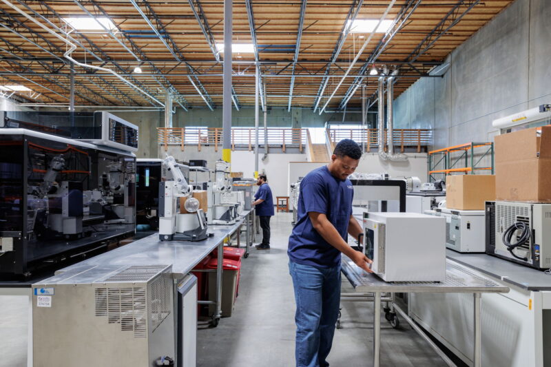 Technician performing a detailed assessment of lab equipment for resale potential in a warehouse setting.